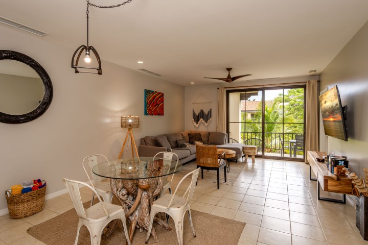 Modern living room with dining area, glass table, gray sofa, wall art, and balcony view.