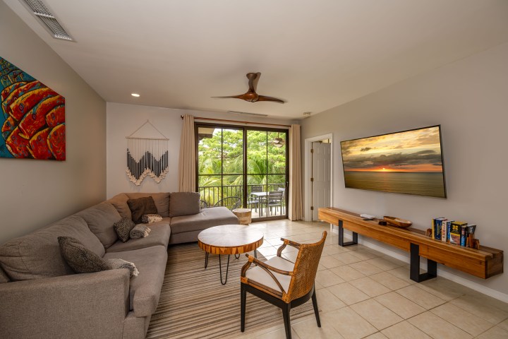 Modern living room with a sectional sofa, wall-mounted TV, and large window view.