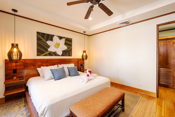 Cozy bedroom with a double bed, wooden accents, pendant lights, and floral artwork.