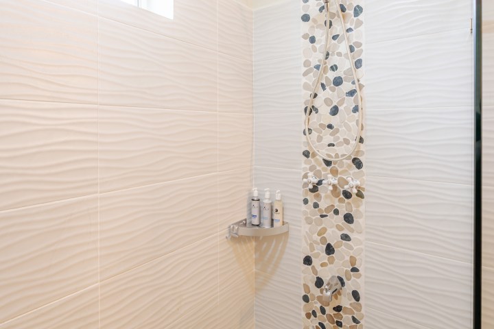 Modern shower with pebble tile strip, beige walls, and small window.