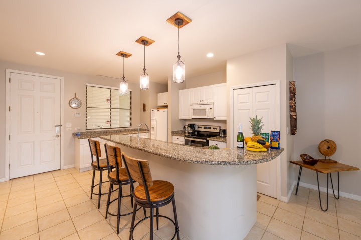 Modern kitchen with granite island, three bar stools, and hanging lights.