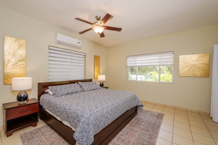 Bedroom with a king bed, ceiling fan, two lamps, and abstract wall art.