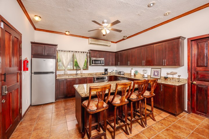 Wooden kitchen interior with island, bar stools, and ceiling fan.