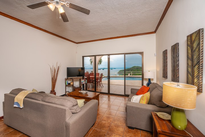 Living room with sofas, TV, ceiling fan, sea view through sliding doors to patio.