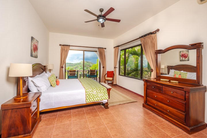Cozy bedroom with wooden furniture, bed, dresser, mirror, and large window with scenic view.
