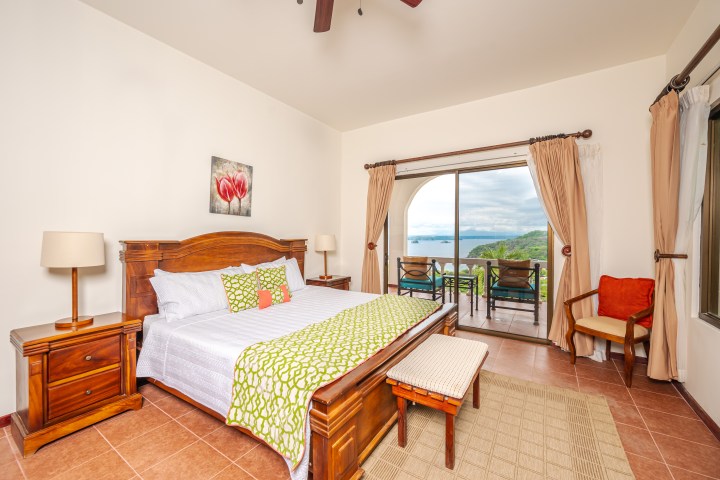 Bedroom with wooden furniture, large bed, ocean view through sliding glass doors and a small balcony.