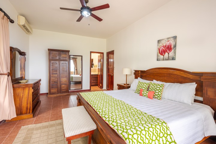 Bedroom with wooden furniture, white bedding, and green accents, ceiling fan, and floral artwork on wall.