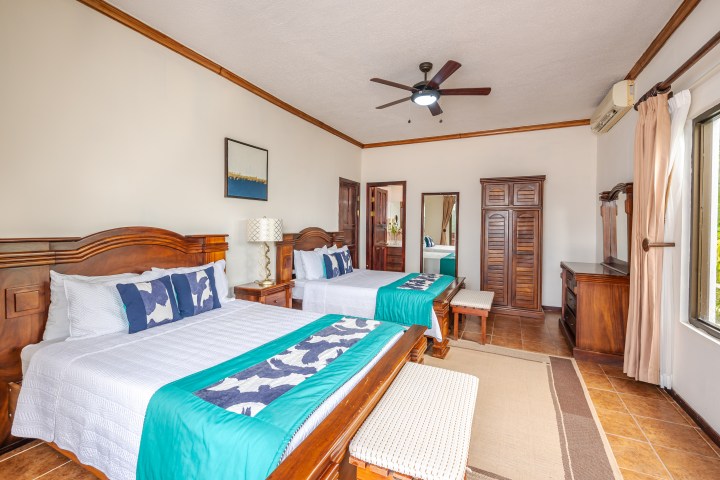 Room with two beds, wooden furniture, ceiling fan, and large window with curtains.