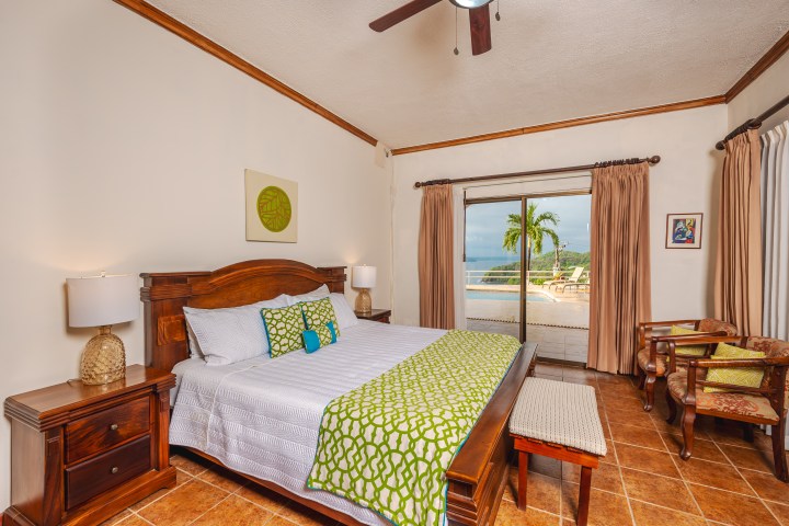 Cozy bedroom with a wooden bed, green accents, and a balcony view of palm trees.