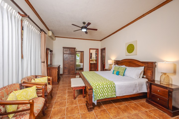 Spacious bedroom with wooden furniture, king bed, armchairs, and ceiling fan.