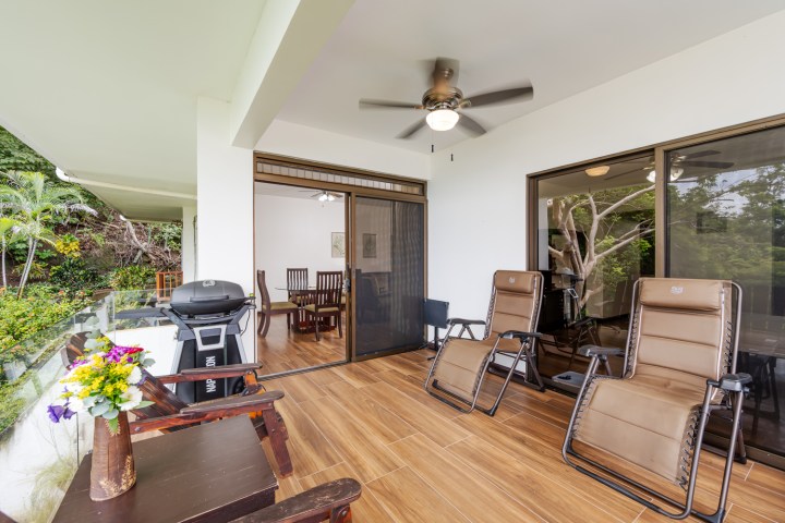Outdoor patio with two recliners, a grill, and a dining area, surrounded by greenery.