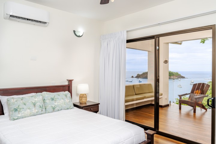 Bedroom with sliding glass doors opening to a balcony with ocean view and lounge chair.