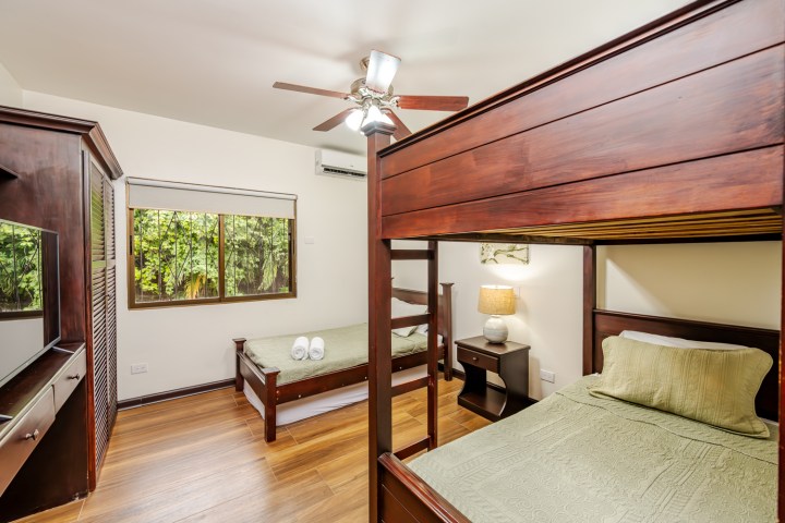 Room with bunk bed, single bed, wooden furniture, and window with garden view.