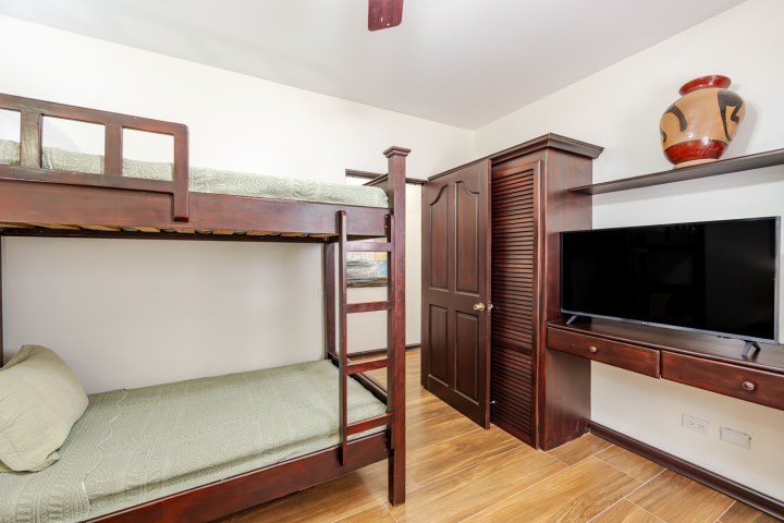 Room with wooden bunk beds, TV, cabinet, and decorative pot on shelf.