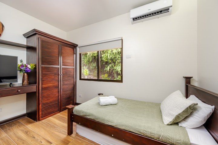 Small bedroom with a single bed, green bedding, wooden furniture, window, and air conditioner.