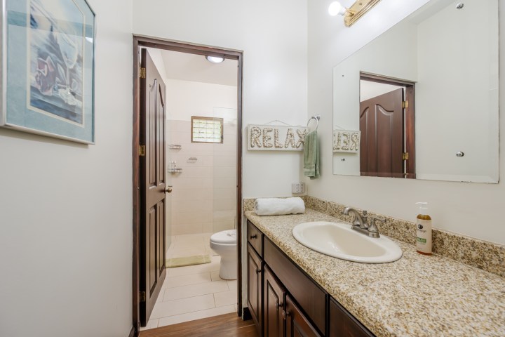 Bathroom with a granite countertop, sink, mirror, and open door leading to toilet and shower.