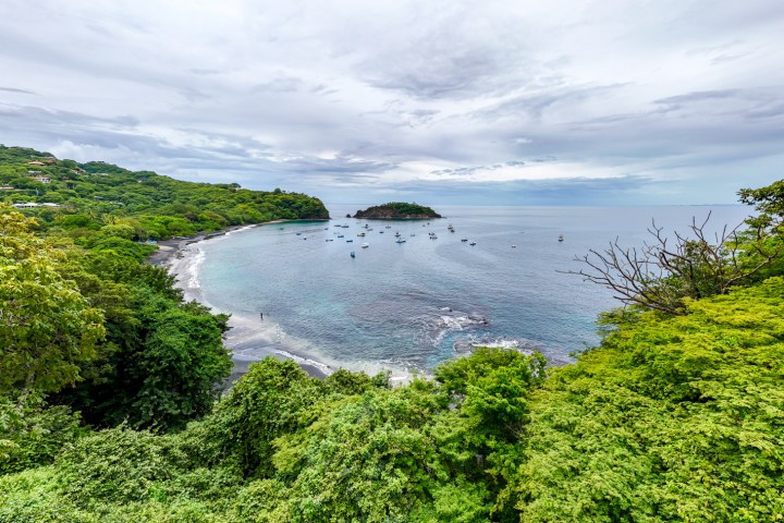 Scenic bay with lush greenery, calm waters, and moored boats under a cloudy sky.