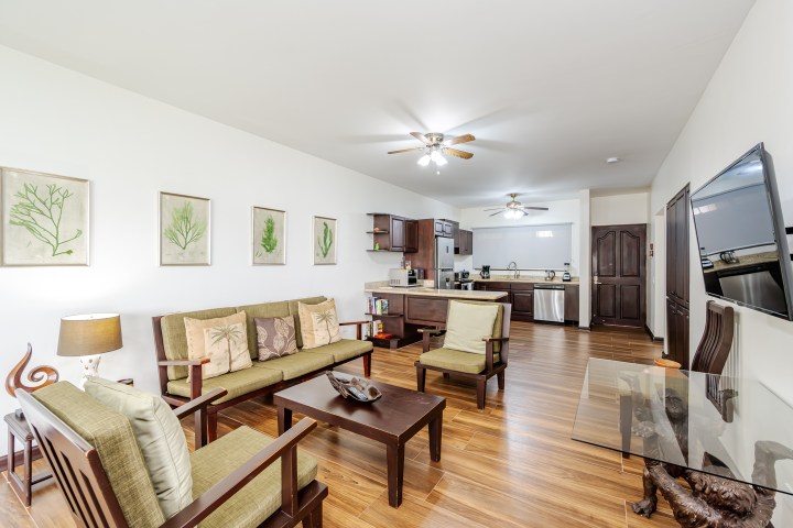 Open-plan living room and kitchen with wooden furniture and ceiling fans.