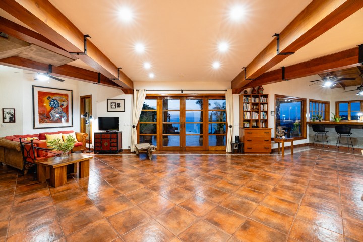 Spacious living area with tiled floor, wooden beams, glass doors, and varied seating.