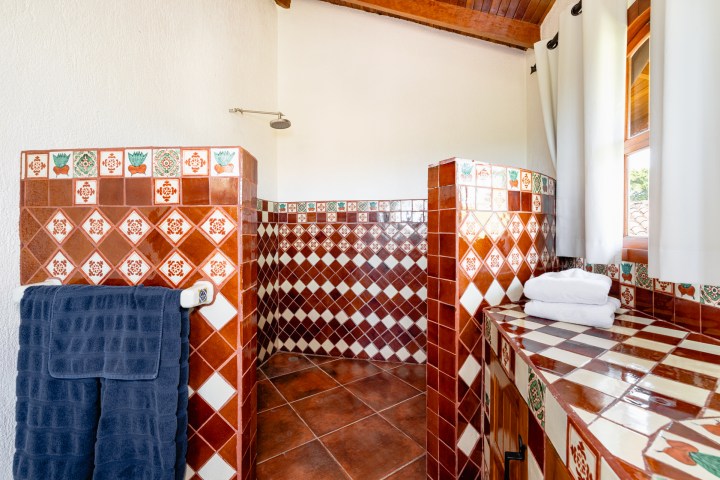Bathroom with brown patterned tile, shower, navy towel, and folded white towels on countertop.