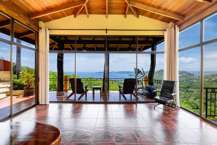 Spacious room with wooden ceiling, large windows, ocean view, and patio with chairs.