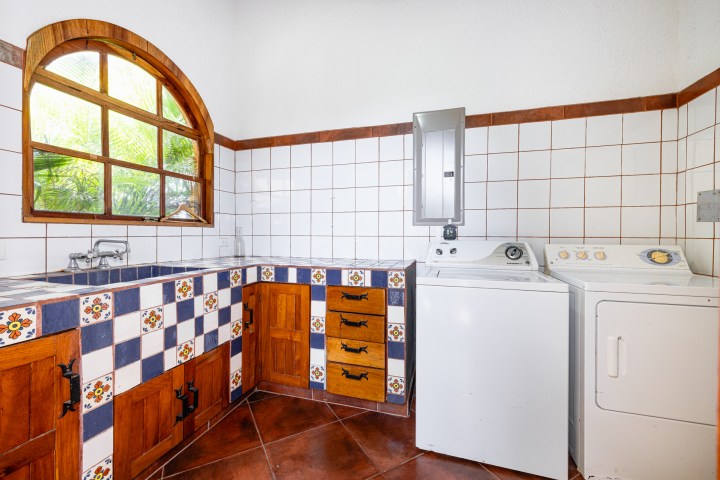 Laundry room with a washer, dryer, tiled counter, wooden cabinets, and an arched window.