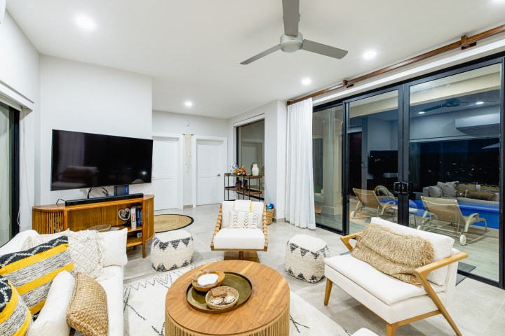 Modern living room with sofas, round table, TV, and large windows showing outdoor patio.