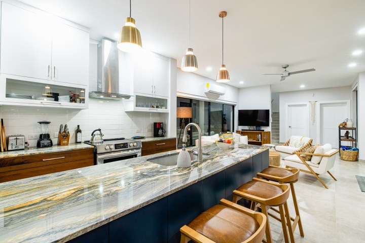 Modern kitchen and living area with marble island, bar stools, and pendant lights.