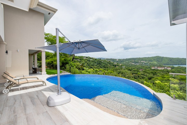 Infinity pool with umbrella, lounge chairs, and scenic hillside view.