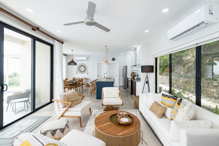 Modern open-plan living area with sofas, dining table, kitchen, and large windows.