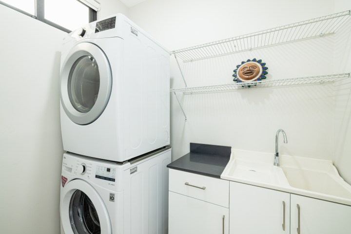 Laundry room with stacked washer and dryer, sink, and metal shelves.