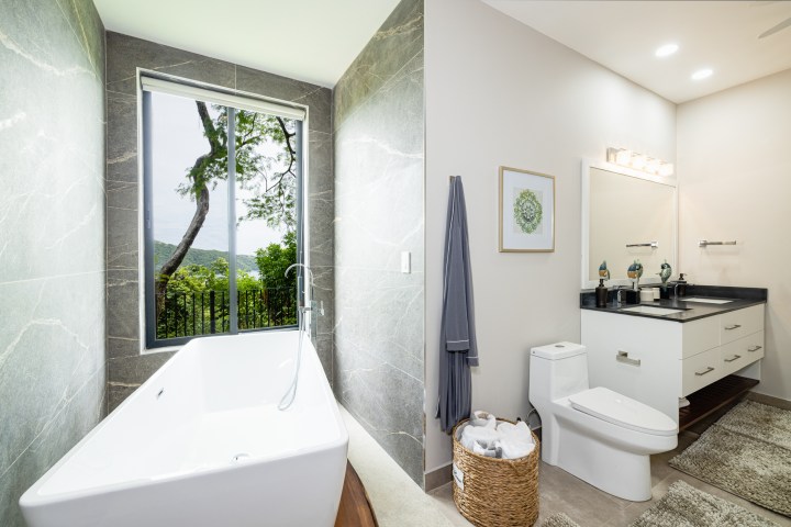 Modern bathroom with tub, large window view, vanity, and toilet.