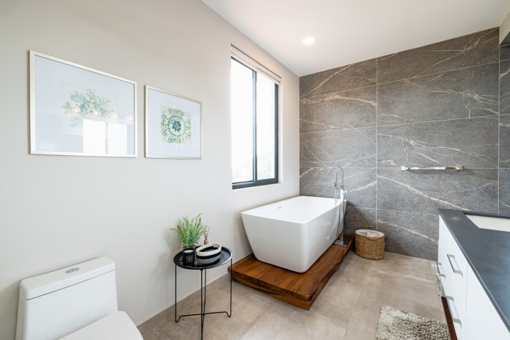 Modern bathroom with bathtub, framed art, and dark stone wall tiles.