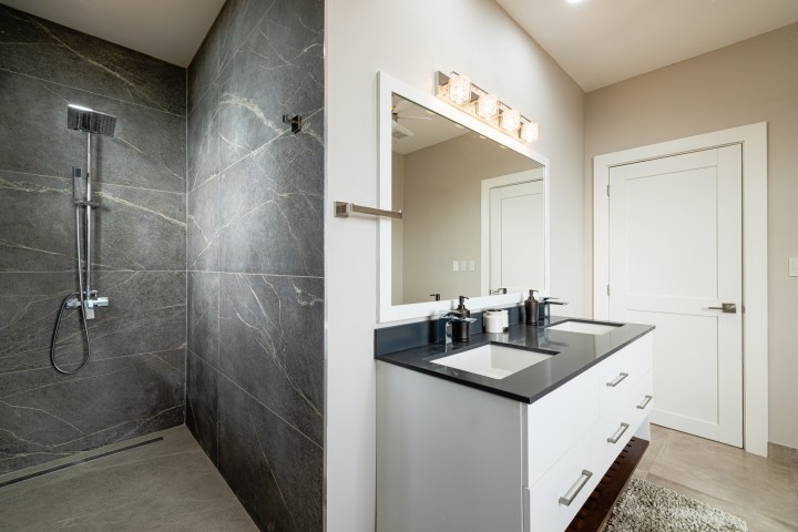 Modern bathroom with large gray tiled shower, double sink vanity, and mirrored cabinet.