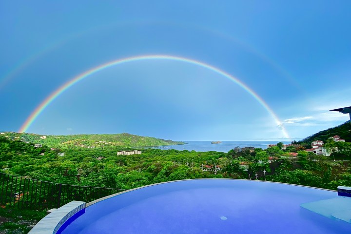 Double rainbow over a coastal landscape with a pool in the foreground.