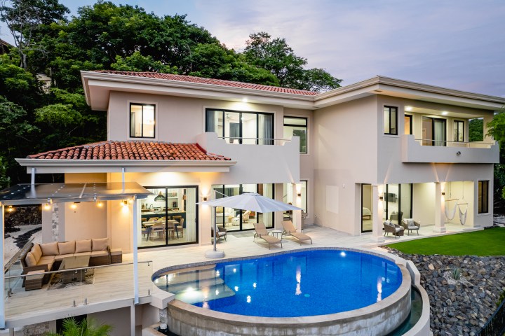 Modern two-story house with pool, patio seating, and large windows.