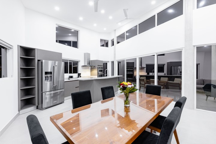 Modern kitchen and dining area with glass table, black chairs, and stainless steel appliances.