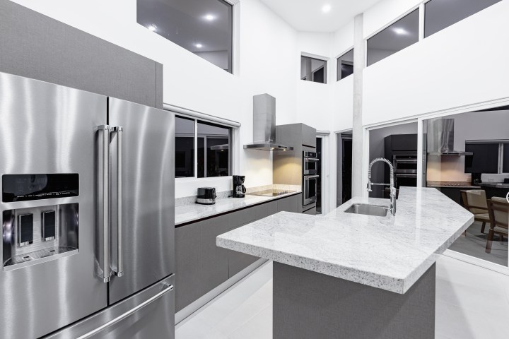 Modern kitchen with stainless steel fridge, island, and grey cabinets.