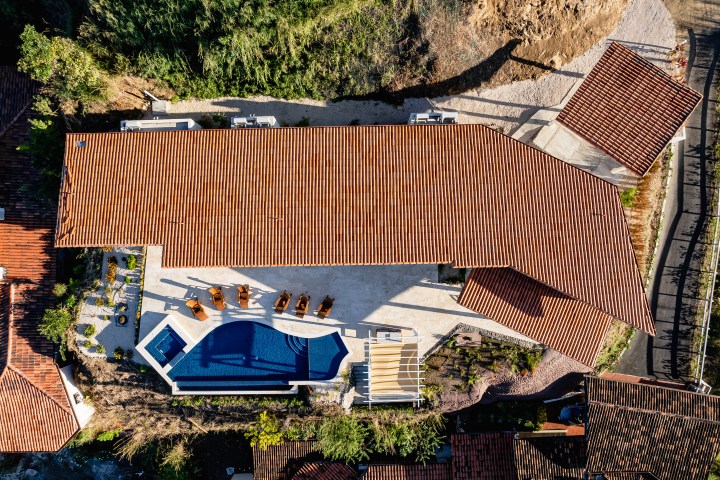 Aerial view of a terracotta-roofed building with a pool and patio chairs.