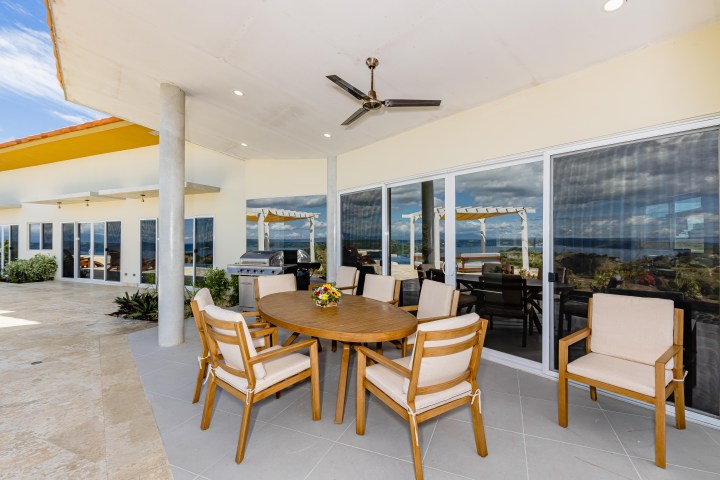 Outdoor patio with a round table, six chairs, BBQ grill, ceiling fan, and scenic ocean view.