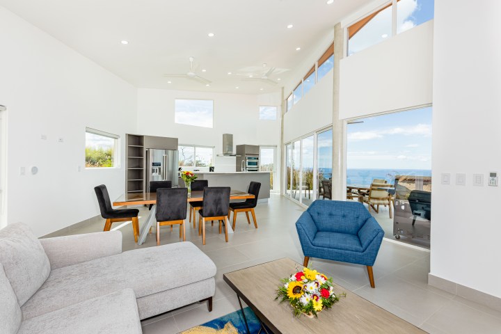 Spacious modern living room with ocean view, large windows, dining table, and cozy furniture.
