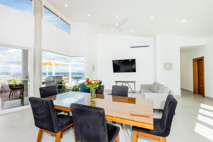 Modern living and dining area with glass table, black chairs, gray sofa, and wall-mounted TV.