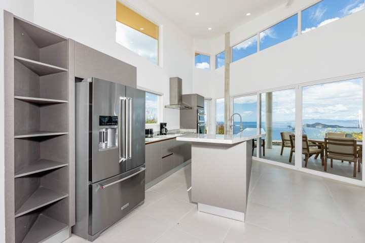 Modern kitchen with island, stainless appliances, and ocean view through large windows.