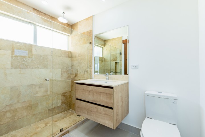 Modern bathroom with glass shower, wooden vanity, and white toilet.
