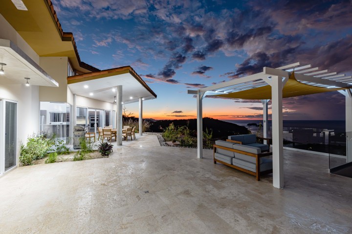 Patio with furniture overlooking ocean and sunset, modern home design.