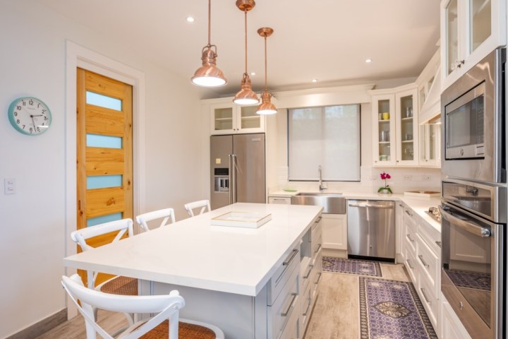 Modern kitchen with white cabinets, island, stainless steel appliances, and three hanging pendant lights.