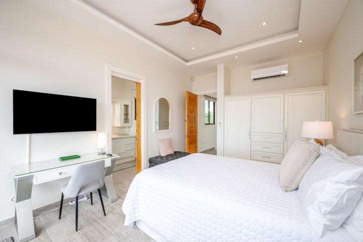 Modern bedroom with white bed, TV, desk, chair, ceiling fan, and wardrobe.