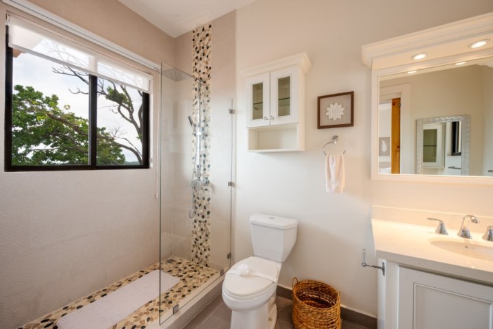 Bright bathroom with a glass shower, toilet, and vanity with mirror and lights.