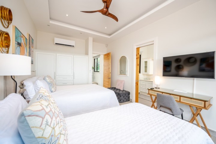 Modern bedroom with two beds, TV, desk, and bathroom entrance.