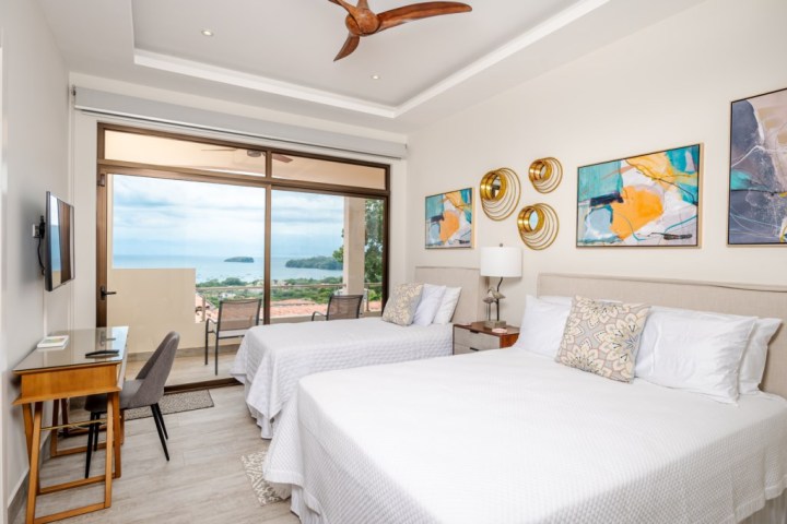 Modern bedroom with two beds, wall art, and a balcony view of the ocean.